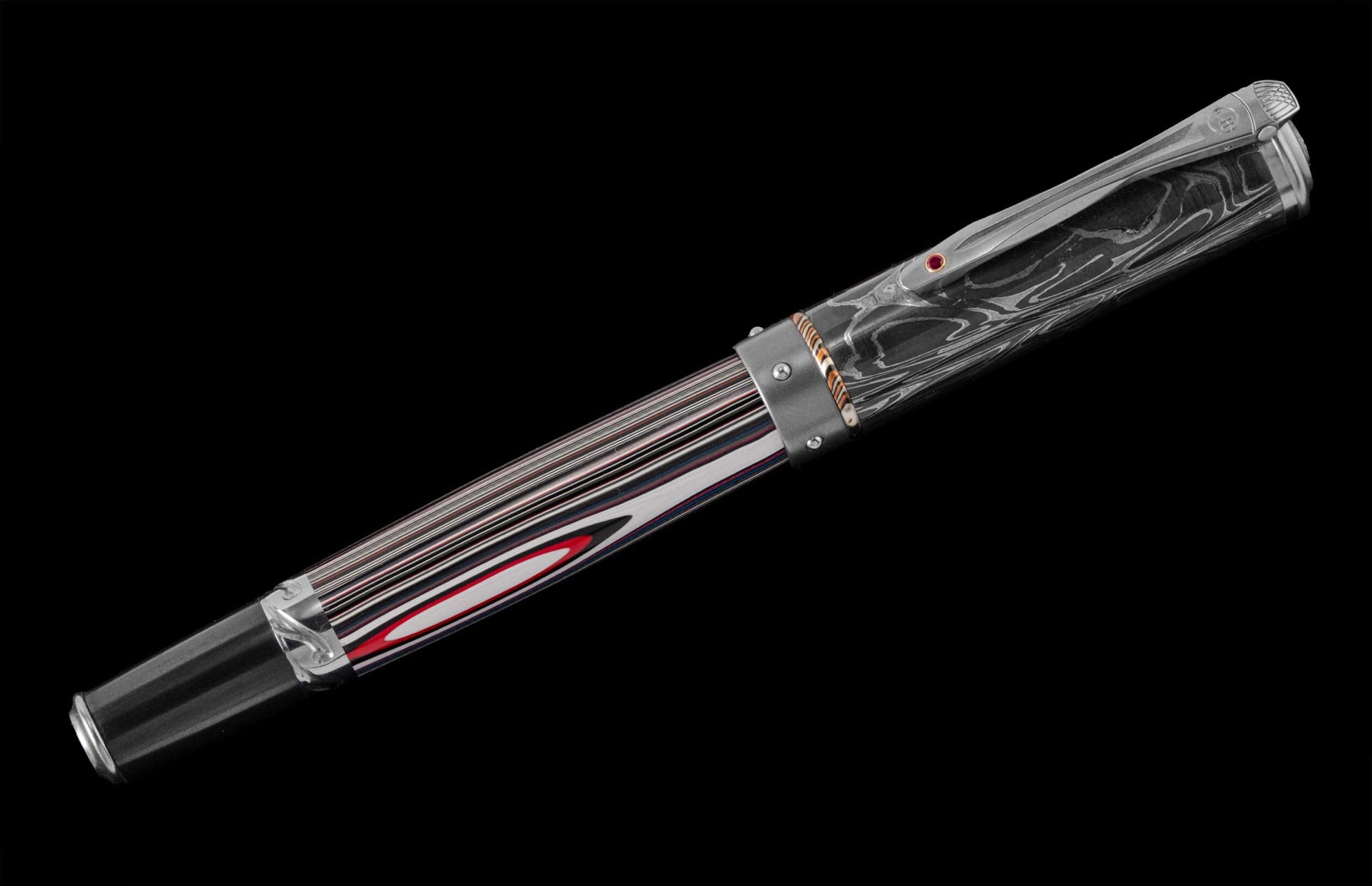 Handcrafted rollerball pen from William Henry featuring a barrel in 'Fordite', and titanium and aluminum. The accents on the carbon fiber cap are in titanium and damascus, the pocket clip is set with a ruby gemstone.